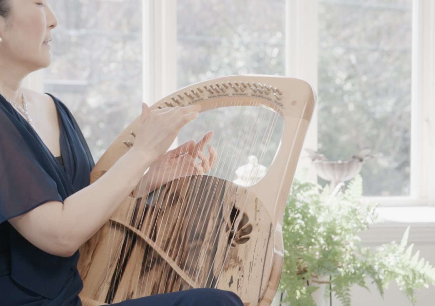 女性がライアーを演奏している写真。光が差し込み透明感がある。